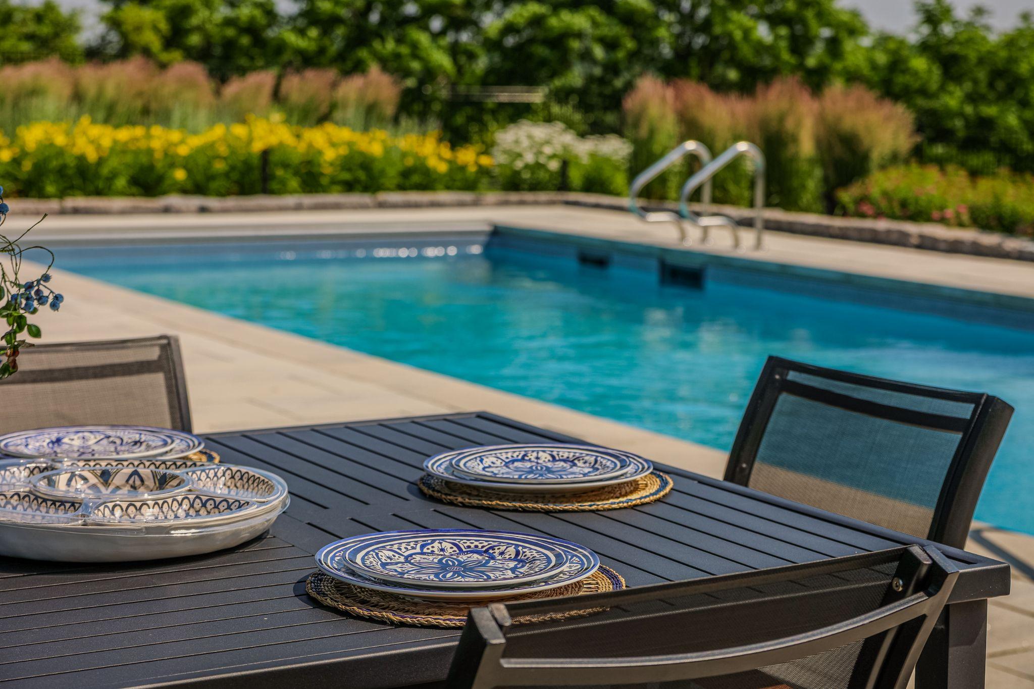 An outdoor dining setup by a pool for its residential landscaping.
