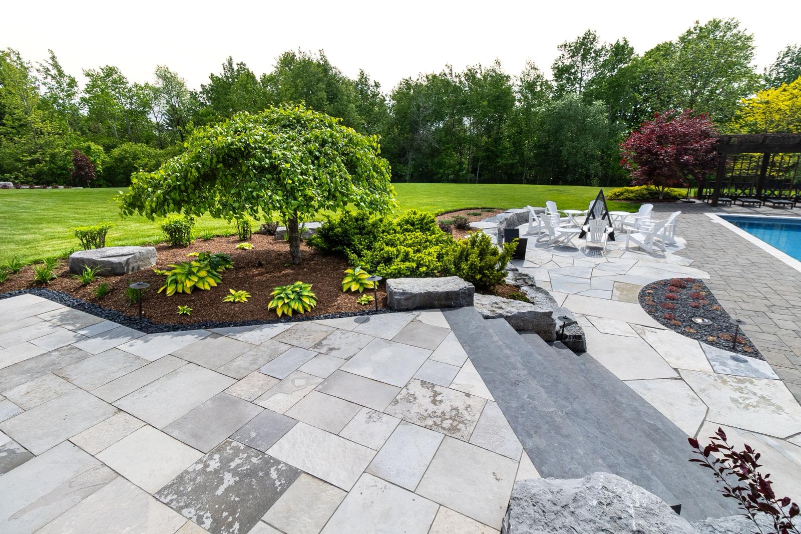 A stone patio with a green lawn behind it and a fire pit.