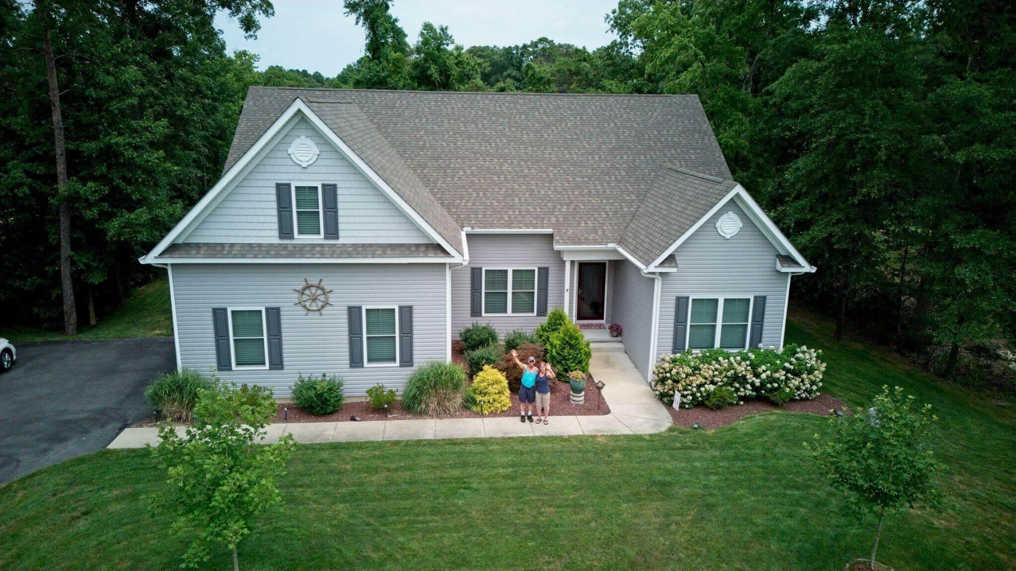 Two people in front of a house with a well-landscaped yard.
