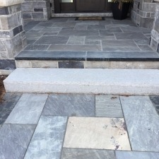 A stone-tiled entrance with steps leads to a doorway, bordered by brick walls and a potted plant on the side.