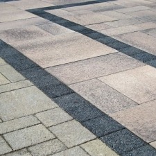 Close-up of a textured, patterned sidewalk with light and dark stone tiles. No people or landmarks visible in the image.