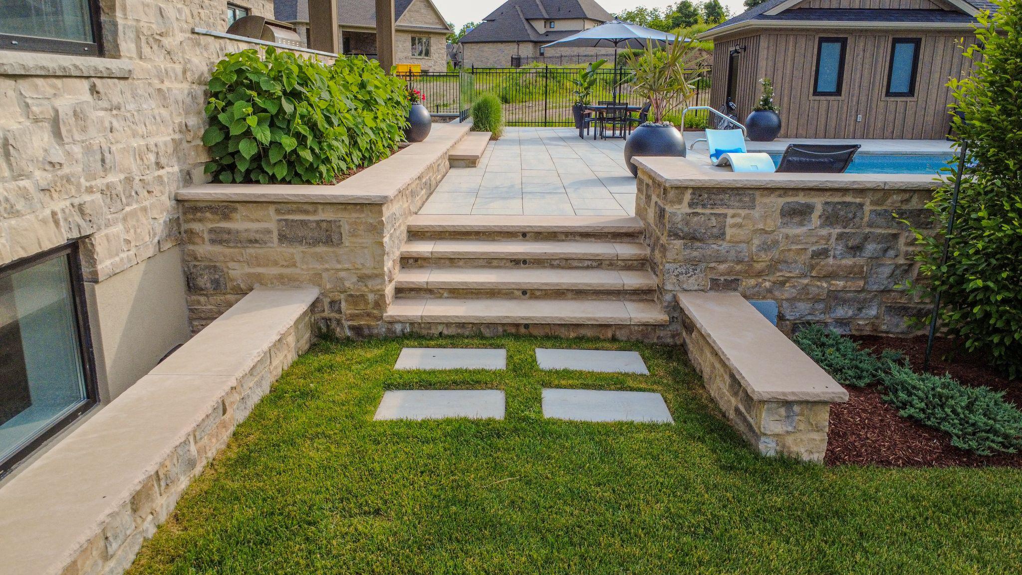 A stone patio with steps leading to a pool made beautiful through routine landscape maintenance.