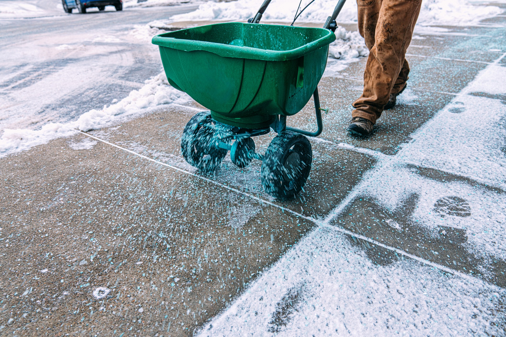 A person uses a spreader to disperse salt on a snowy sidewalk, preventing ice formation and ensuring safe pedestrian passage.