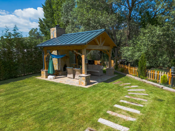 A peaceful backyard with a wooden gazebo, stone path, and a fenced area surrounded by green trees and well-maintained grass.